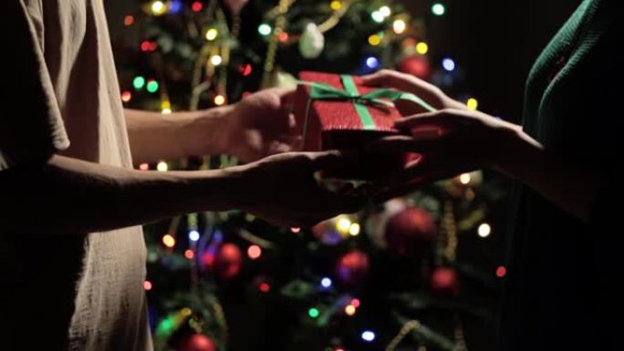 他给了她一份用红纸包裹的大礼物，上面绑着一条绿色的丝带，背景是一棵模糊的新年树。家庭聚会，圣诞节，爱