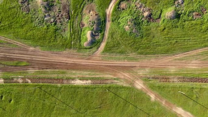 绿色的田野和山丘上点缀着一条土路和立交，乡村地区，带有摄像头的无人机沿着它们的高度移动，俯视图。农村