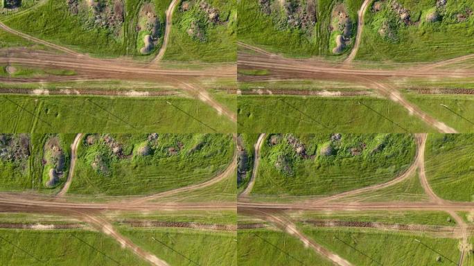 绿色的田野和山丘上点缀着一条土路和立交，乡村地区，带有摄像头的无人机沿着它们的高度移动，俯视图。农村