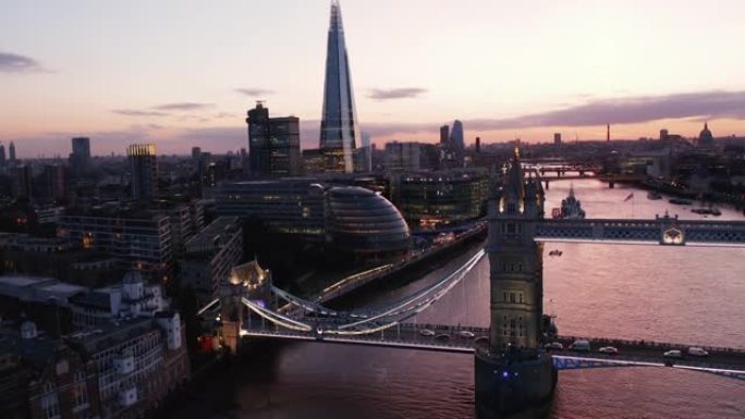 上升泰晤士河上塔桥的晚间镜头。市政厅和岸上碎片摩天大楼的现代建筑。水面反射粉红色的黄昏天空。英国伦敦