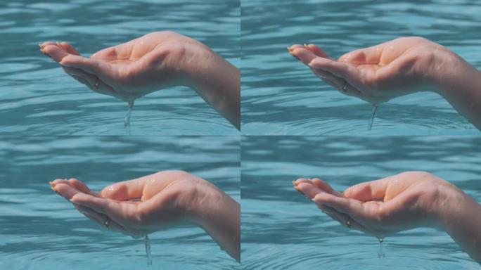 女性手玩水的特写镜头，在阳光明媚的日子用手指抓住并倒入水池。人类手掌舀水，水滴落在水面