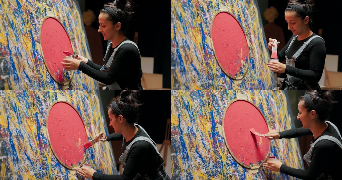 微笑的女人站在画架附近，画布上正在创作最新的展览绘画。女人努力完成杰作，用附加的圆形模板的红色油漆填