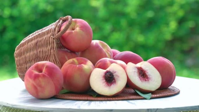 新鲜的桃子在模糊的绿色背景上切成薄片，桃子水果在花园的木桌上的竹篮中。