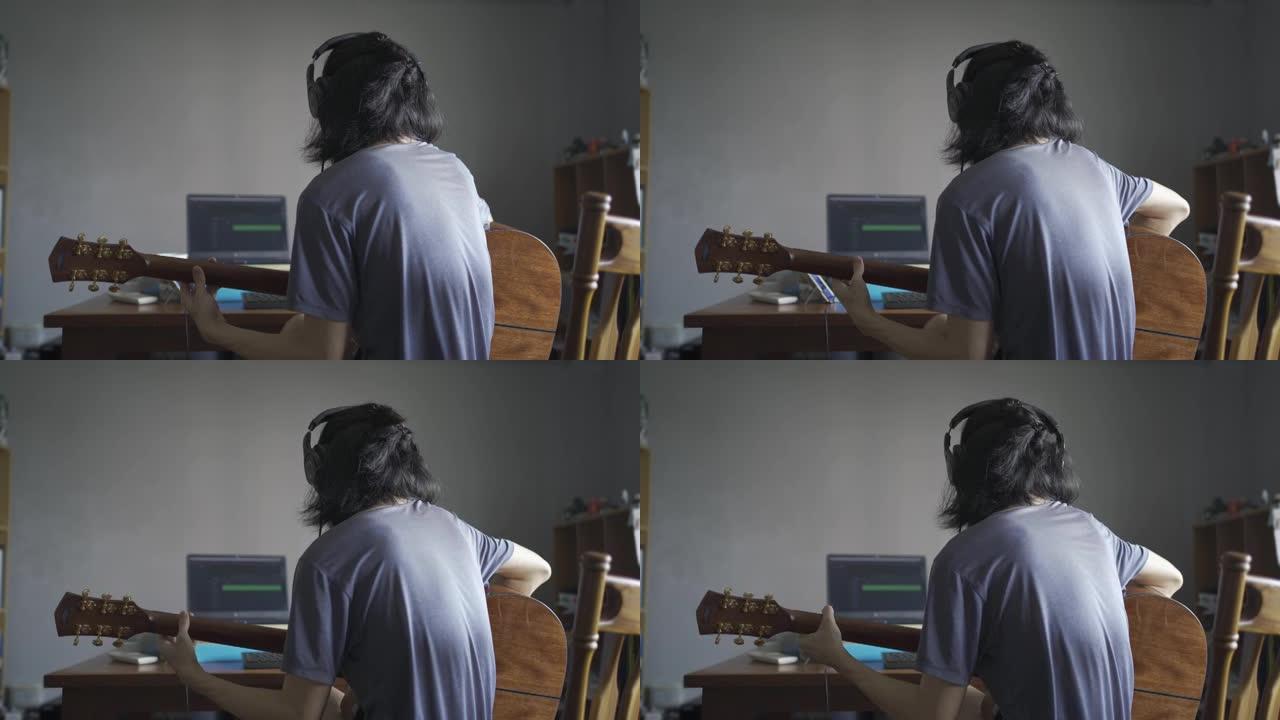 一个留着长发的男人戴着耳机，弹木吉他，以便在家庭房间里录音到计算机中
