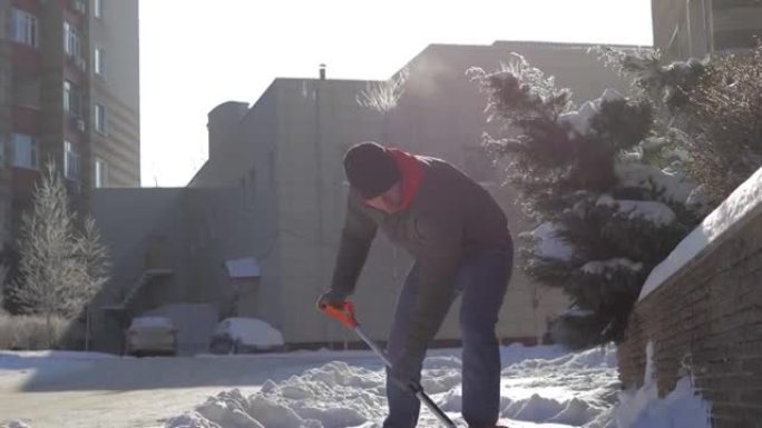 一个男人在院子里晴朗的晴天打扫雪。那家伙用铁锹手动从街上铲起白雪。冬季工作和清除深层积雪，铲起，扔在