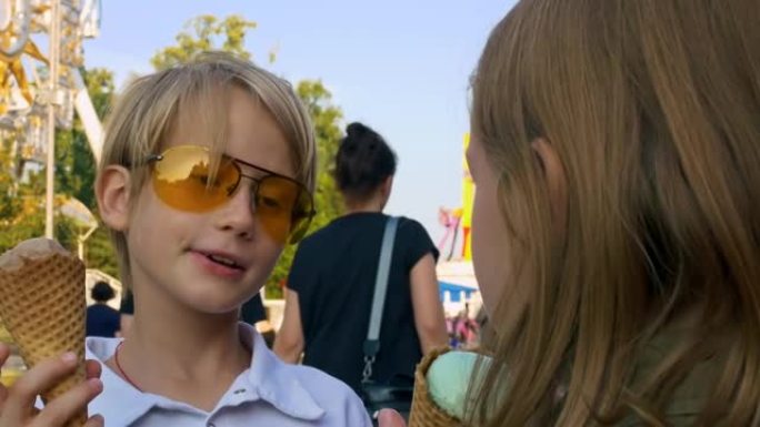 一个男孩和一个金发女孩在游乐园里吃冰淇淋。在年度博览会上快乐的青少年童年。儿童摄入过多的糖会导致糖尿