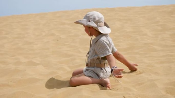 男孩正穿着旅行者的衣服坐在沙丘上