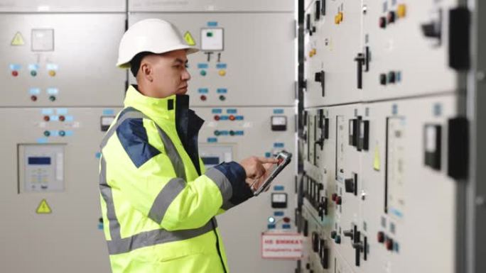 亚洲男子电气工程师将平板电脑监控电气系统放在控制室。技术人员检查制造工业工厂发电的控制面板屏幕系统