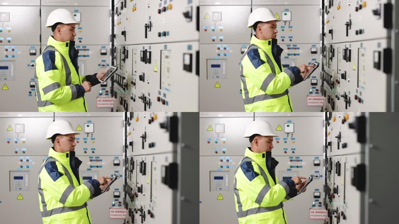 亚洲男子电气工程师将平板电脑监控电气系统放在控制室。技术人员检查制造工业工厂发电的控制面板屏幕系统