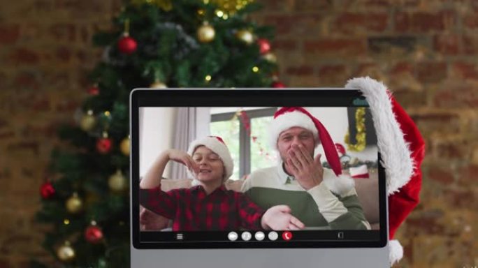 快乐的父亲和儿子在计算机上的视频通话中挥舞着圣诞装饰品和树