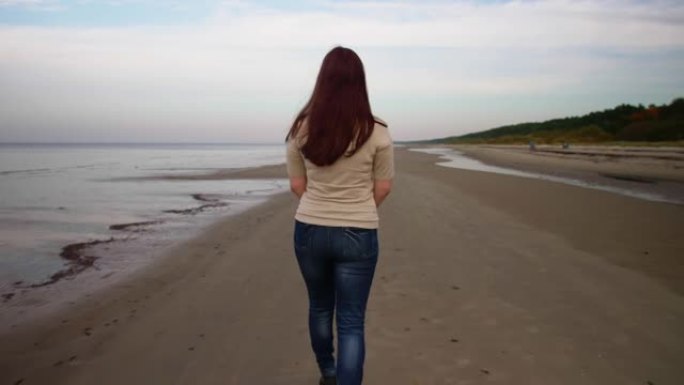 地道的女人沿着海边散步，从后面看。