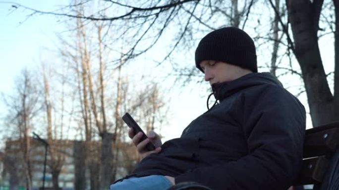 年轻的白人男子坐在城市背景下的长凳上使用智能手机。