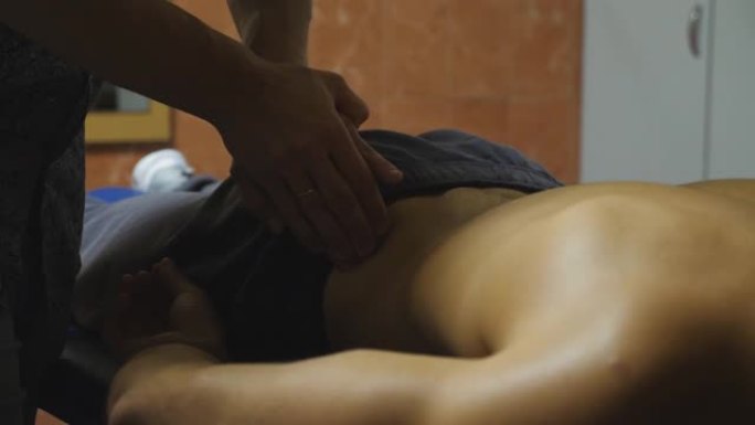 男按摩师的手在客厅按摩年轻运动员的腰。专业按摩师在艰苦训练后放松和振兴运动员的肌肉。健康生活方式的概
