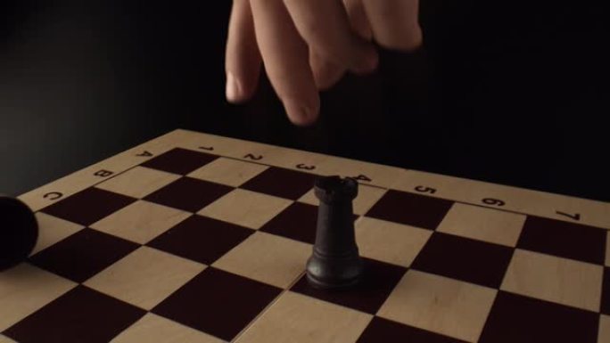 国际象棋比赛的最后阶段。将死。玩家手里拿着一只象棋车，撞倒了国王的身影。深色背景上的木制棋盘。