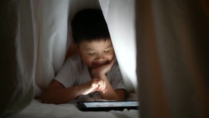 亚洲男孩在卧室的毯子下使用数字平板电脑