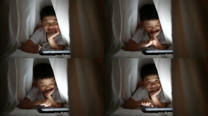 亚洲男孩在卧室的毯子下使用数字平板电脑