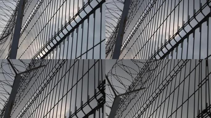 高监狱栅栏与带刺铁丝网，底部视图。监狱栅栏，迎着晴朗的天空。自由的概念