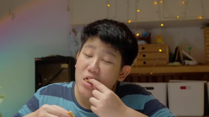 亚洲男孩晚上在家吃饼干，万圣节概念。