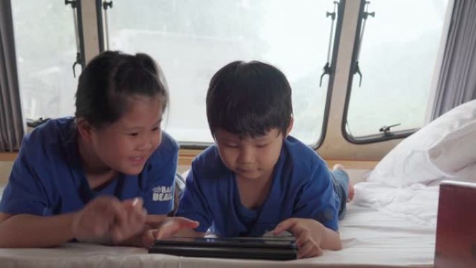 亚洲兄弟姐妹在大篷车上使用平板电脑。当他们在夏日躺在前面时。房车假日旅行
