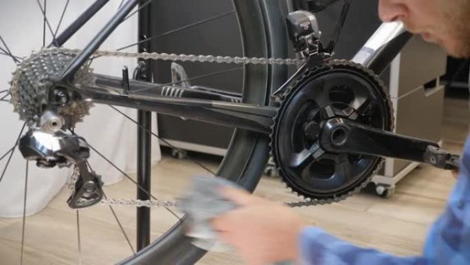 自行车维护。自行车机械师用超细纤维布清洁自行车链条。男性双手用布清洁自行车链条。自行车车间