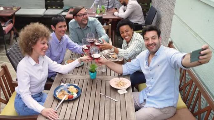 现代多种族的同事在餐厅享用午餐时用红酒敬酒时自拍