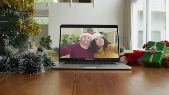 在圣诞节视频通话中戴着圣诞老人帽子的微笑夫妇在笔记本电脑上