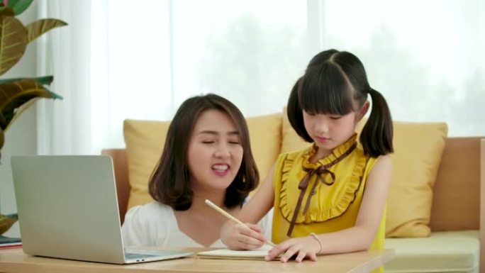 亚洲母亲帮助女儿在家做家庭作业。