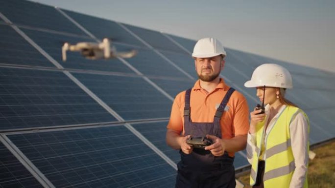 光伏太阳能发电厂戴着头盔和控制无人机的工业专家。太阳能电池板阵列安装。技术和生态。女性投资者检查工作
