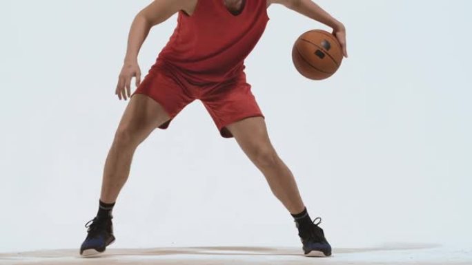 球技运球篮球运动员在工作室的白色背景。一个穿着红色运动服的高个子年轻运动员在地板上击球。特写。慢动作