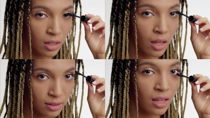 非裔美国年轻女子在睫毛上涂上睫毛膏，白色背景