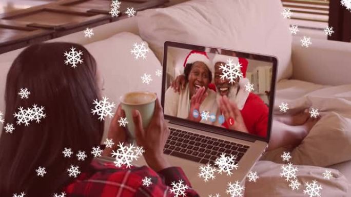 圣诞节期间，雪花落在拿着咖啡杯的女人身上，在笔记本电脑上放着录像带