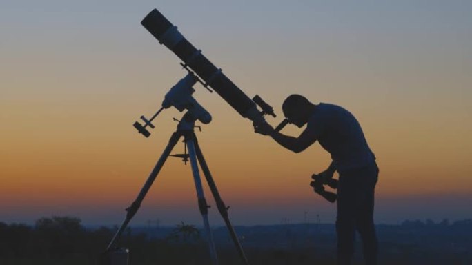 星空下的男人，望远镜和乡村的轮廓。