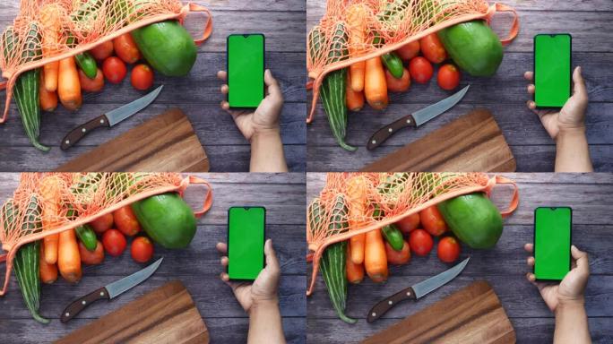 男子手持智能手机的俯视图，桌上摆放着新鲜蔬菜