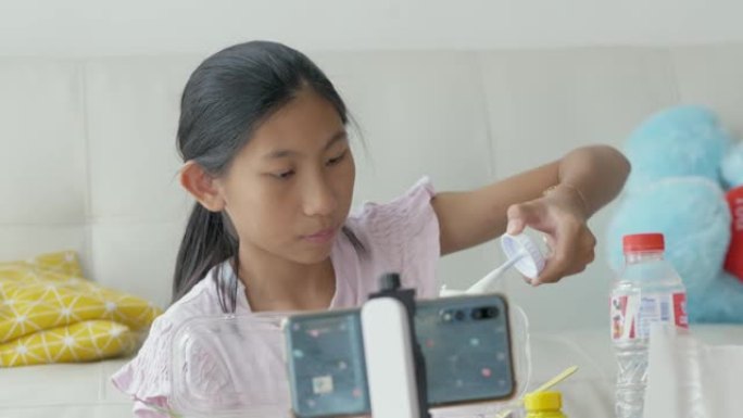 亚洲女孩通过智能手机制作视频，有关如何制作黏液或黏土的内容。新一代生活方式概念。