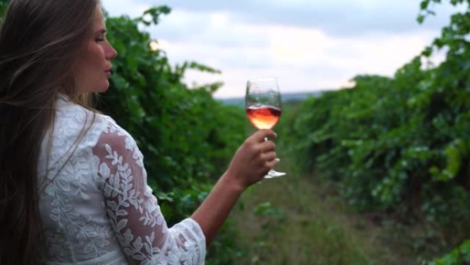 一个漂亮的女人在葡萄园日落时拿着一杯红酒。女性的手微微摇晃着红酒的玻璃杯。葡萄酒测试和葡萄酒酿造概念