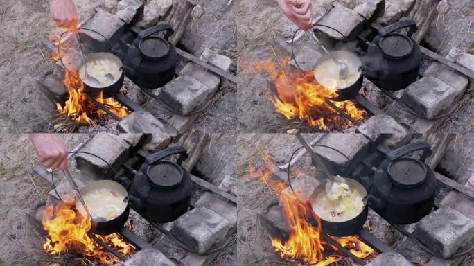 男性在户外树林里的篝火上的平底锅里准备食物。缩放。特写