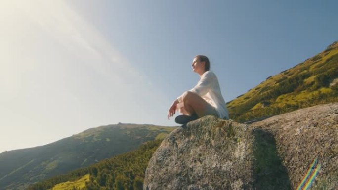 女孩运动员坐在山上的一块岩石上，看着大自然的美丽。在山中旅行，感受美丽