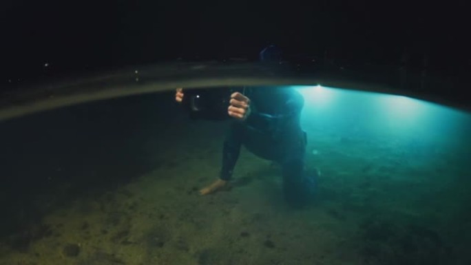 夜湖水下摄影师。穿着潜水衣的年轻女子带着水下相机潜水，晚上在湖里拍照