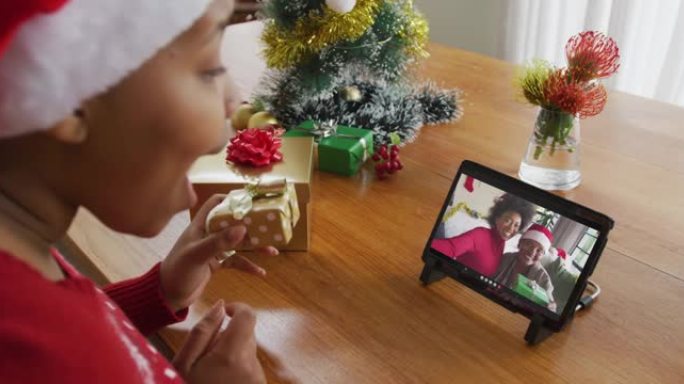 戴着圣诞老人帽子的非洲裔美国妇女使用平板电脑进行圣诞节视频通话，屏幕上有家人