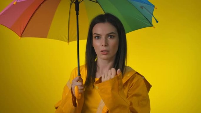 穿着黄色雨衣的忧心忡忡的女人带着彩虹伞正在检查雨水