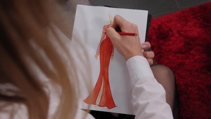 特写艺术家时装设计师用红色铅笔画了一件连衣裙的草图。