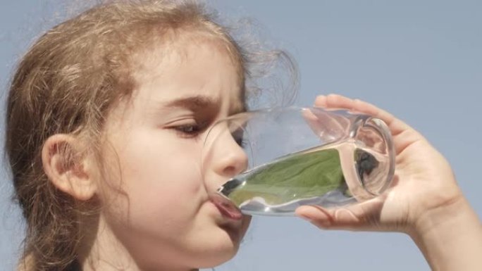 口渴的孩子在户外用玻璃喝水，阳光普照。可爱女孩水杯新鲜透明纯净水慢动作儿童水杯水健康身体护理健康生活