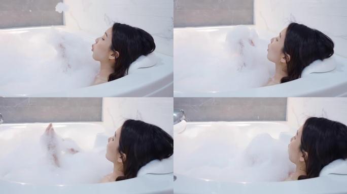 特写开朗的亚洲女人在浴缸里吹泡沫