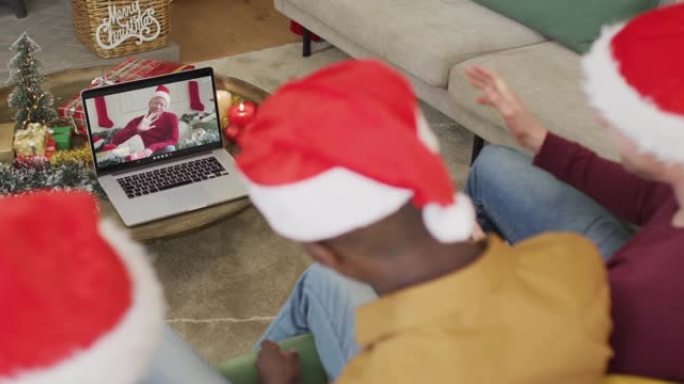 带有圣诞老人帽子的多元化家庭使用笔记本电脑进行圣诞节视频通话，屏幕上有男人