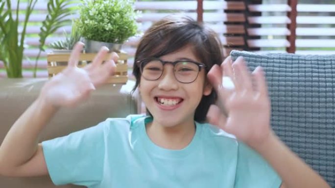 幸福亚洲男孩问候手挥手打招呼视频肖像，亚洲男孩戴眼镜手挥舞问候相机打招呼或打招呼视频通话在家概念