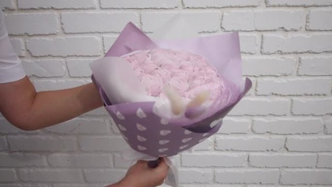 一名妇女展示了用工艺纸包装的棉花糖花束。棉花糖玫瑰花。