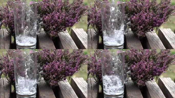 在秋天的花园中，将矿泉水倒入干燥的薰衣草和石南花背景上的玻璃杯中，慢动作