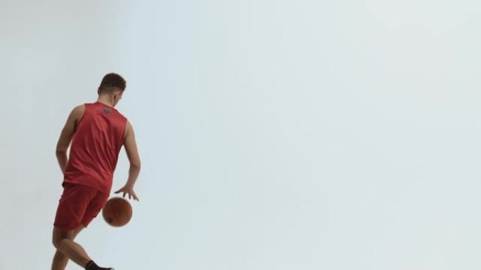 侧视图或穿着红色运动服的年轻篮球运动员在白色工作室背景下奔跑和运球。运动员正在训练中准备比赛。慢动作