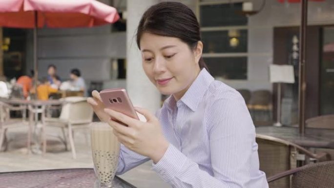 穿着衬衫的慢动作亚洲女商人用稻草喝泡泡奶茶在亚洲台湾流行的当地糖果。年轻的女上班族放松户外咖啡馆，用