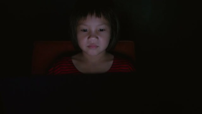 女孩在晚上使用笔记本电脑或数字平板电脑设备。